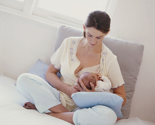 Woman sitting cross legged, supporting the head of a young baby with her hand and breastfeeding